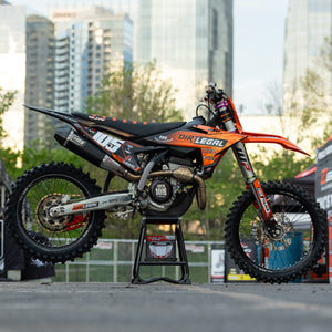 Moto da cross arancione e nera su una Risk Racing F.F.S. stare con il paesaggio urbano sullo sfondo