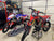 two motocross dirt bikes in a garage. One is sitting on an RR1 Ride on Lift and Factory pit mat and the other is on an ATS adjustable top stand. MX equipment by Risk Racing.
