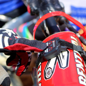 Close up of a Holeshot wireless remote attached to the handlebar padding of a dirt bike. Gloved MX riders finger about to hit one of the two buttons.